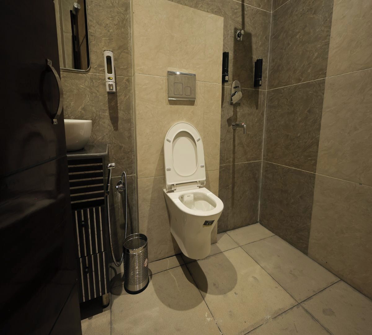A modern bathroom with a toilet, a hand dryer, a trash can, and a shower area.