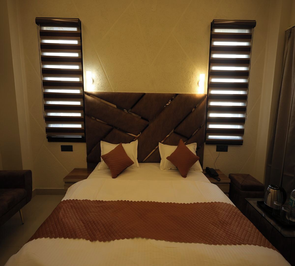 A hotel room with a large bed, two bedside tables, a nightstand, and a wall-mounted lamp.