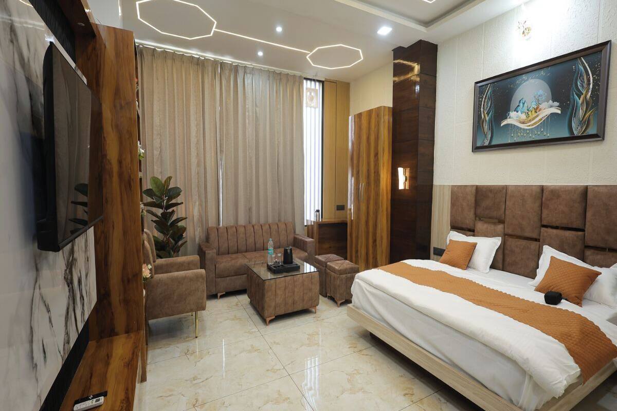 A modern hotel room with a large bed, a sofa, a coffee table, and a TV mounted on the wall.