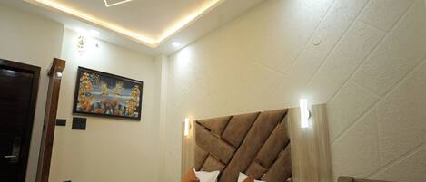 A modern bedroom with a large bed, a ceiling fan, recessed lighting, and a painting on the wall.