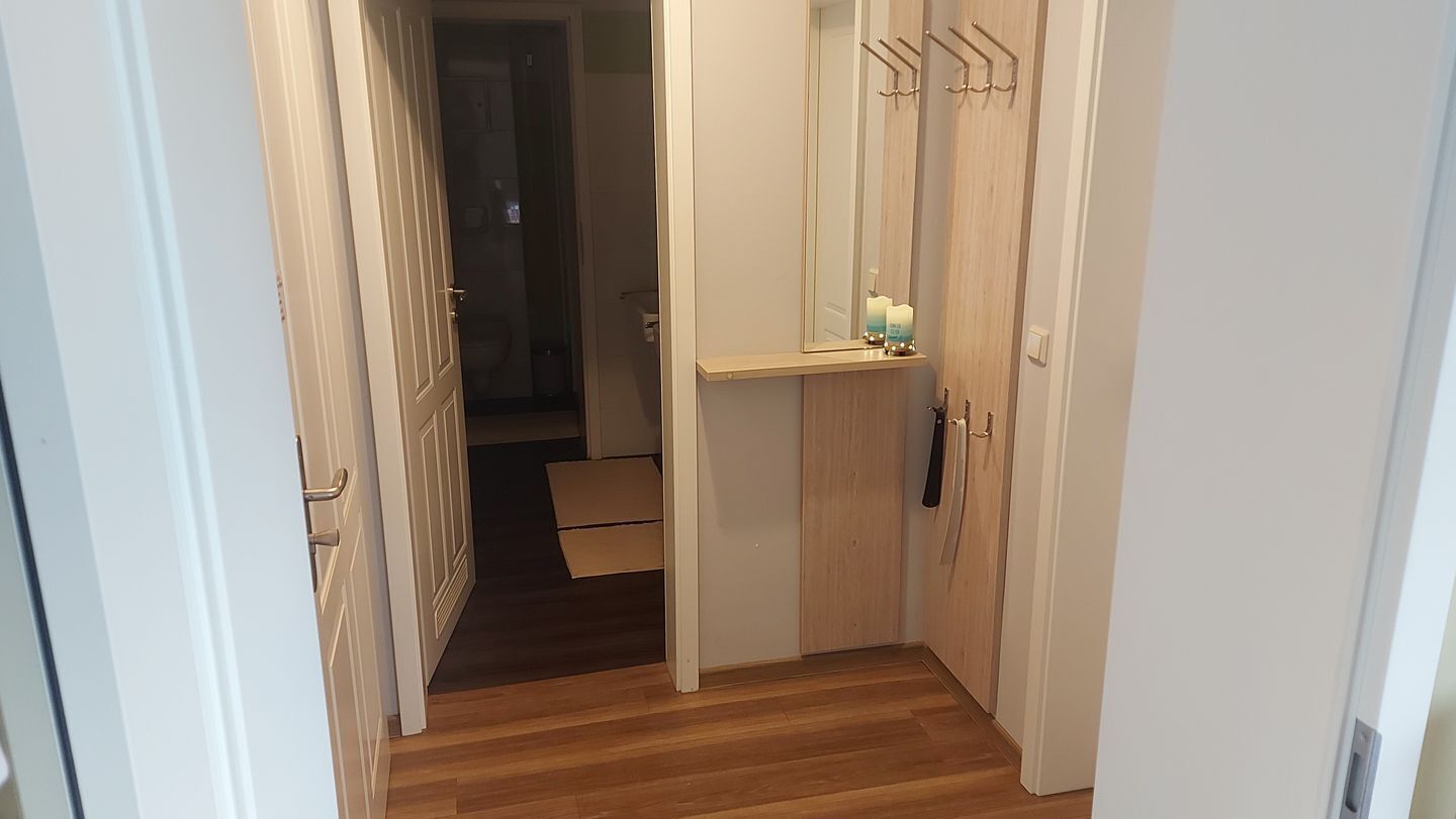 Un corridoio con pavimento in legno, una porta con portasciugamani e uno specchio appeso al muro.