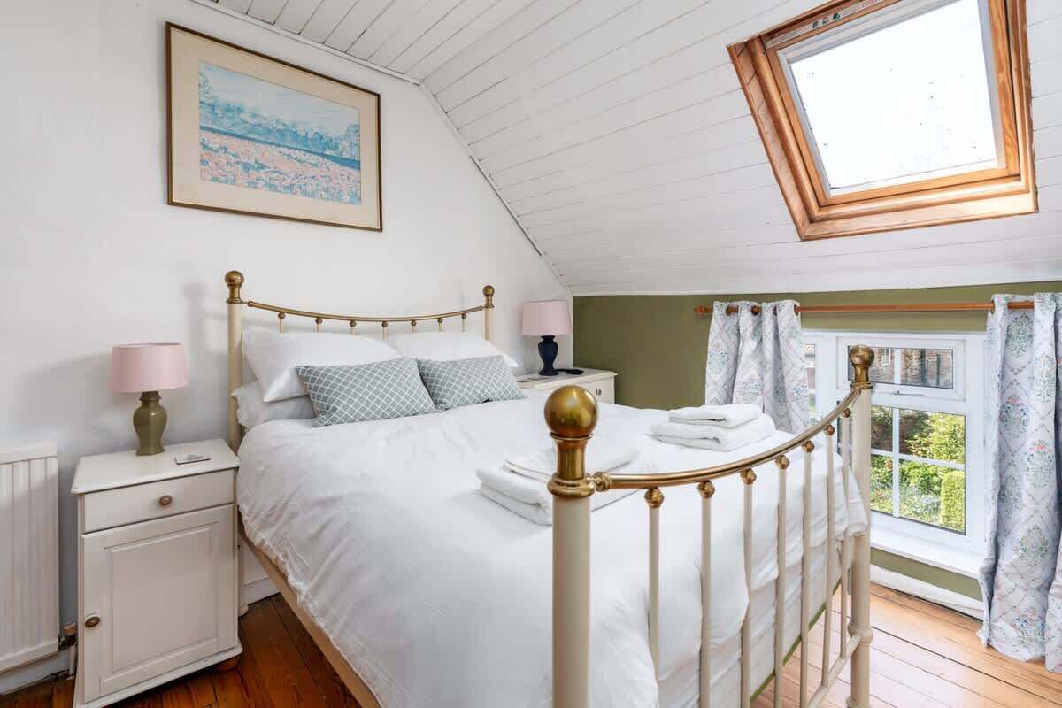 Une chambre à coucher avec un lit, des tables de chevet, une fenêtre avec des rideaux, un puits de lumière et un tableau au mur.