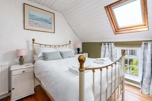 A bedroom with a bed, nightstands, a window with curtains, a skylight, and a painting on the wall.