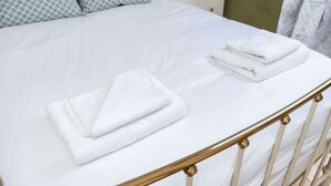 A bed with white bedding, a gold-framed headboard, and a nightstand with a lamp and a book.