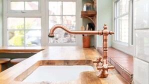 A kitchen with a copper faucet, wooden countertop, and a window with a view of greenery.