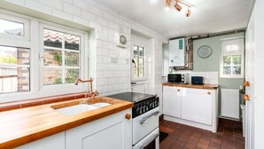 A kitchen with white cabinets, a wooden countertop, a stove, a microwave, and a window.