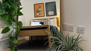 A bedroom with a bed, a large mirror, two framed pictures, and a potted plant. - Wigan 1BR Haven:  Perfect for a Relaxing Stay (Wigan)