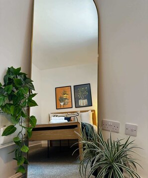 A bedroom with a bed, a large mirror, two framed pictures, and a potted plant.