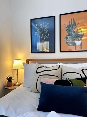 Un lit avec une tête de lit en bois, une lampe de chevet et deux œuvres d’art encadrées représentant des plantes.