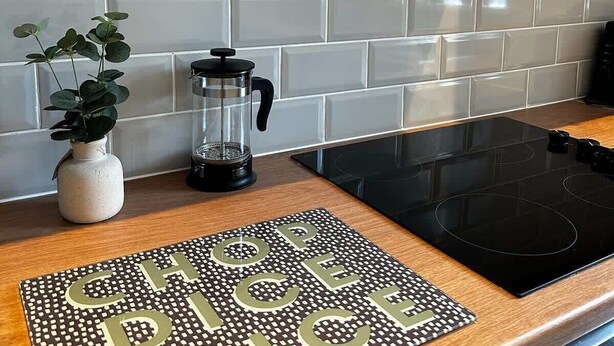 A kitchen with white subway tiles, a black stove, a coffee maker, and a plant. - Wigan 1BR Haven:  Perfect for a Relaxing Stay (Wigan)