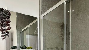 Een moderne badkamer met een douchecabine van glas, een witte wastafel en een spiegel erboven.