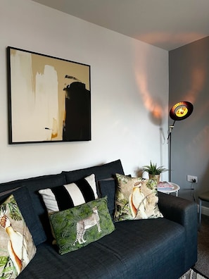 A modern living room with a dark blue sofa, patterned cushions, a floor lamp, and a large abstract painting on the wall.