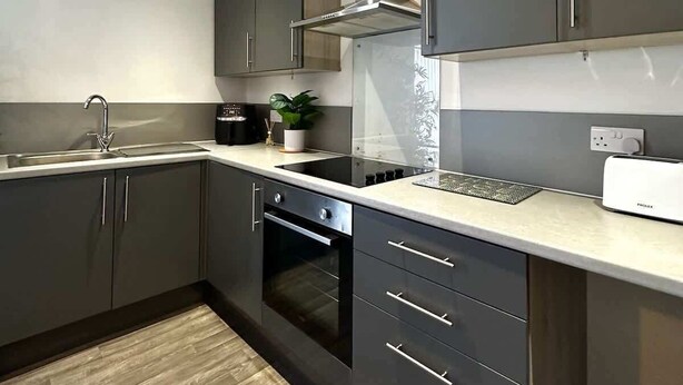 Een moderne keuken met donkere kastjes, een roestvrijstalen afzuigkap, een inbouwoven en een aanrecht met een broodrooster.