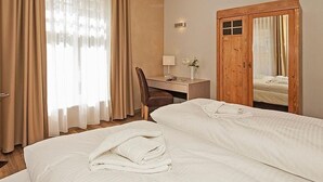 Habitación de hotel con dos camas, un escritorio, una silla y un armario de madera.