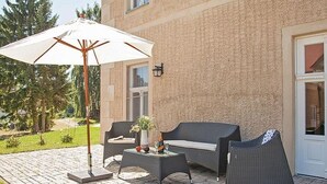 Un patio al aire libre con mobiliario de mimbre, una mesa y una sombrilla.
