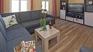 Una sala de estar con un sofá gris, una mesa de centro de madera y un televisor sobre un mueble.