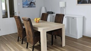 En matplats med ett träbord, fyra stolar, en fruktskål, ett vitt skåp, en lampa och två inramade tavlor på väggen.