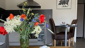 Ein Essbereich mit einem Glastisch, einem Dessertteller mit Kuchen, einer Kaffeetasse und einer Blumenvase.