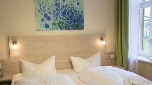 Ein Hotelzimmer mit zwei Betten, einem Holzkopfteil, weißen Bettwäsche und einem Blumenbild an der Wand.