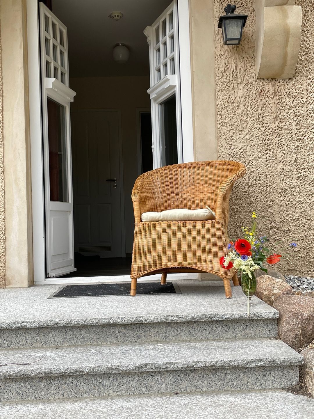 A wicker chair with a cushion on stone steps leading to a door.
