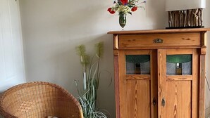 Ein Korbstuhl mit Kissen, eine Holzkommode mit Glastüren und eine Vase mit Blumen darauf.