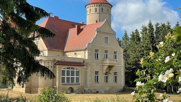 Ein historisches Gebäude mit einem Turm, großen Fenstern und einem roten Ziegeldach.