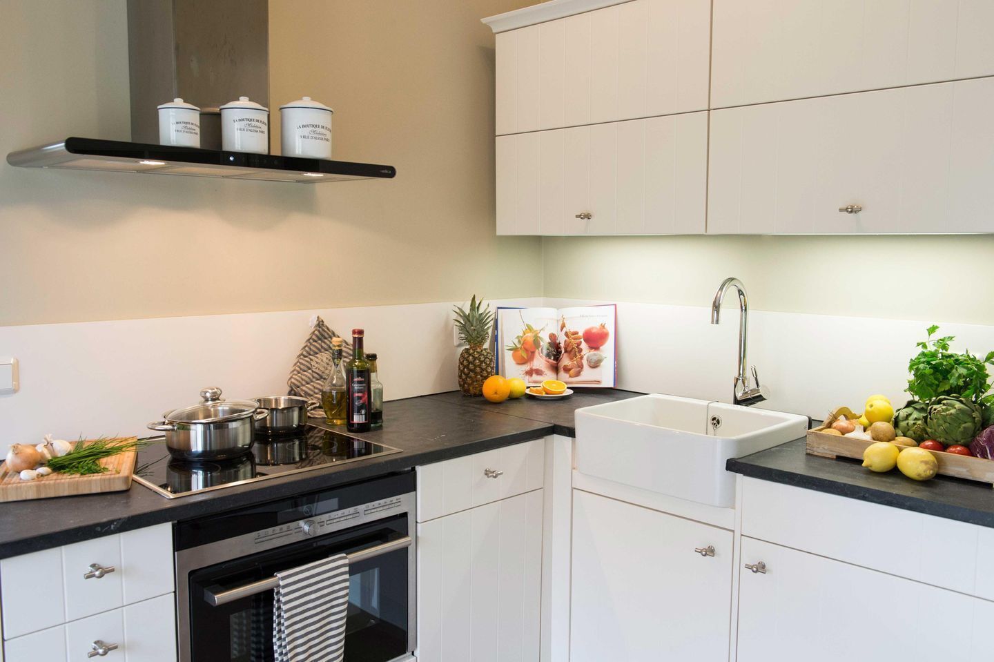 A modern kitchen with white cabinets, a black countertop, a stainless steel stove, and a sink.