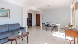 Un salon avec un canapé gris, une table basse en bois et un coin repas comprenant une table et des chaises blanches.
