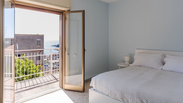 Une chambre à coucher comprenant un lit, une table de chevet, une lampe et une porte-fenêtre coulissante donnant sur un balcon.
