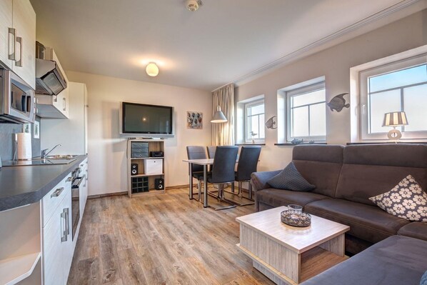 A modern living room with a sofa, a coffee table, and a TV. There is a kitchen area with a microwave, stove, and sink. - Windflüchter LH-305 - The country farm Windflüchter LH-305 - Family-friendly (Stolpe auf Usedom)