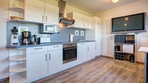 A modern kitchen with white cabinetry, stainless steel appliances, and a flat-screen TV mounted above the counter.