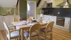 Un coin repas avec une table dressée pour quatre personnes, une cuisine équipée d’appareils modernes et un escalier menant à l’étage supérieur.