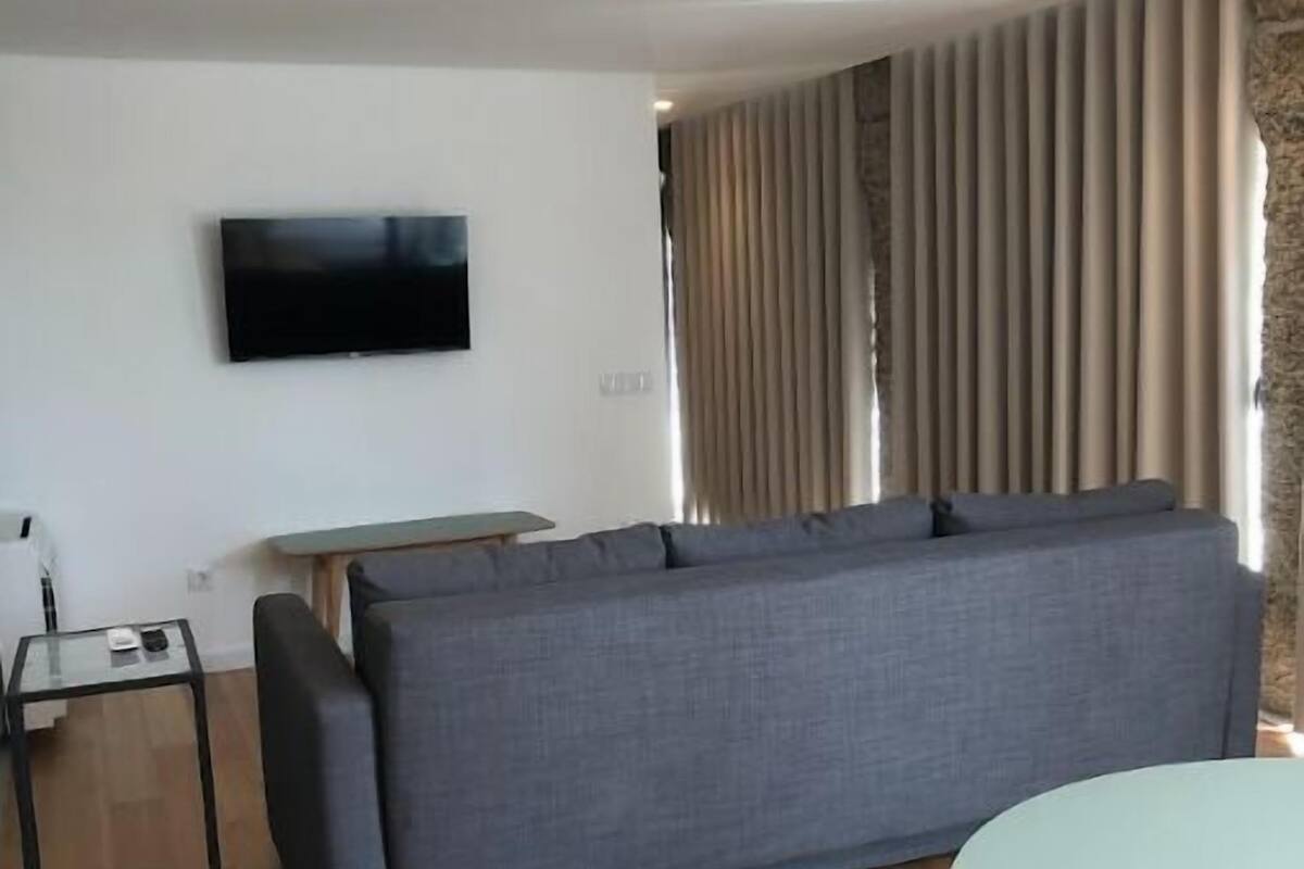 Una sala de estar moderna con un sofá gris, un televisor de pantalla plana montado en la pared, una mesita auxiliar y una mesa redonda con patas de madera.