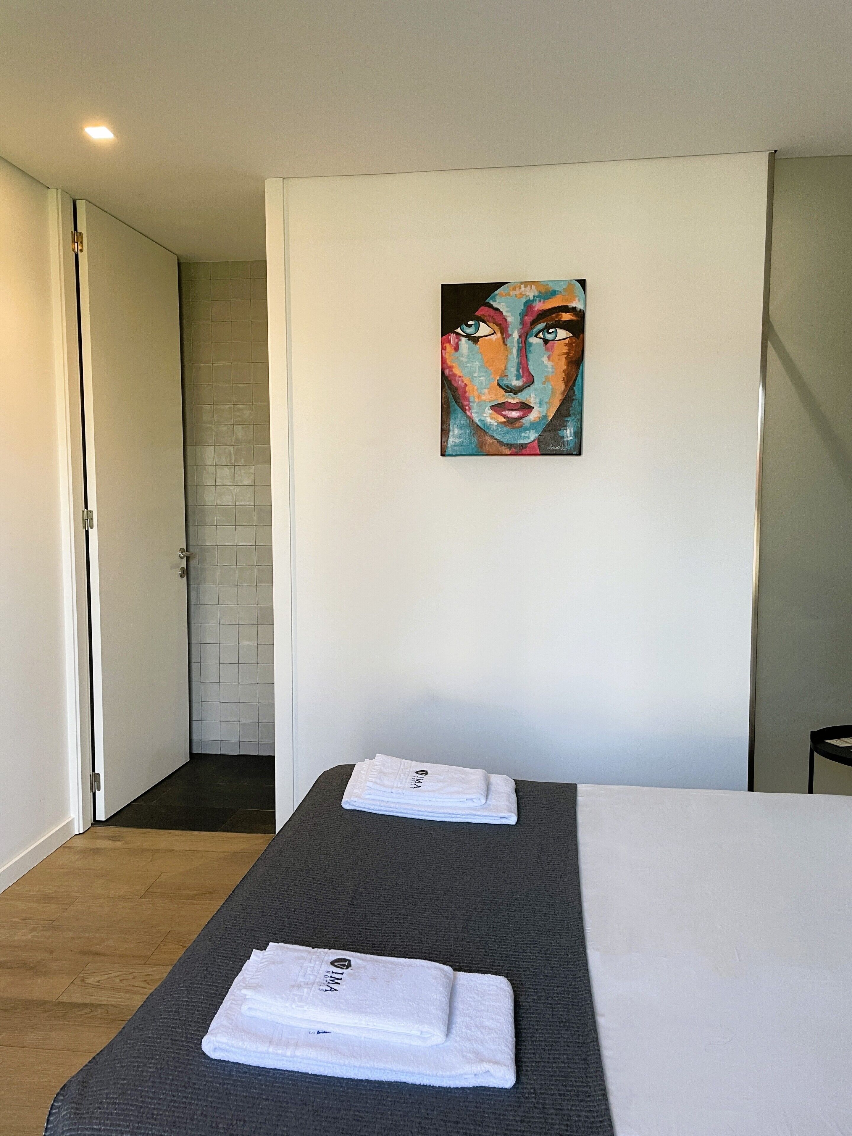 A hotel room with a bed, two towels, a painting on the wall, and a door leading to a bathroom.