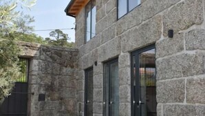 Un edificio de piedra con amplias puertas y ventanas de vidrio, techo de madera y un patio empedrado.