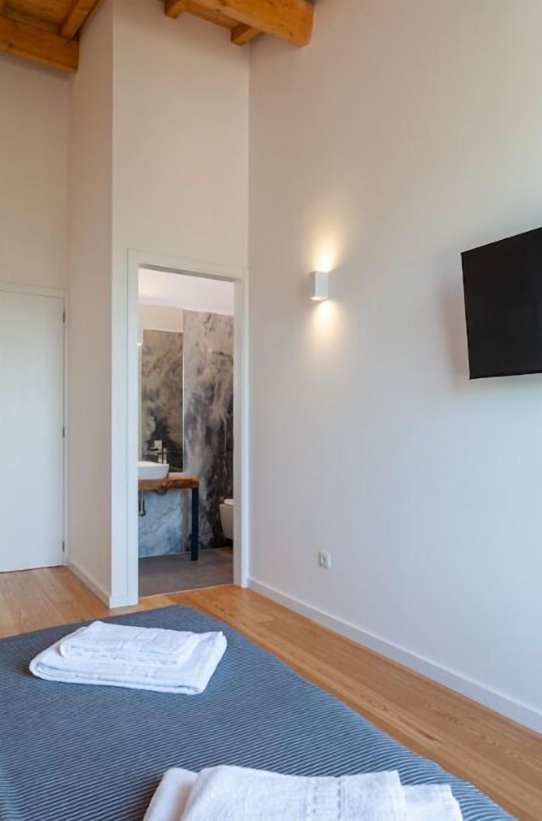Ein Schlafzimmer mit einem Bett, einem an der Wand montierten Fernseher und einem durch eine offene Tür einsehbaren Badezimmer.