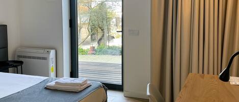 A hotel room with a bed, a wooden table, a TV, and a sliding glass door leading to an outdoor area.