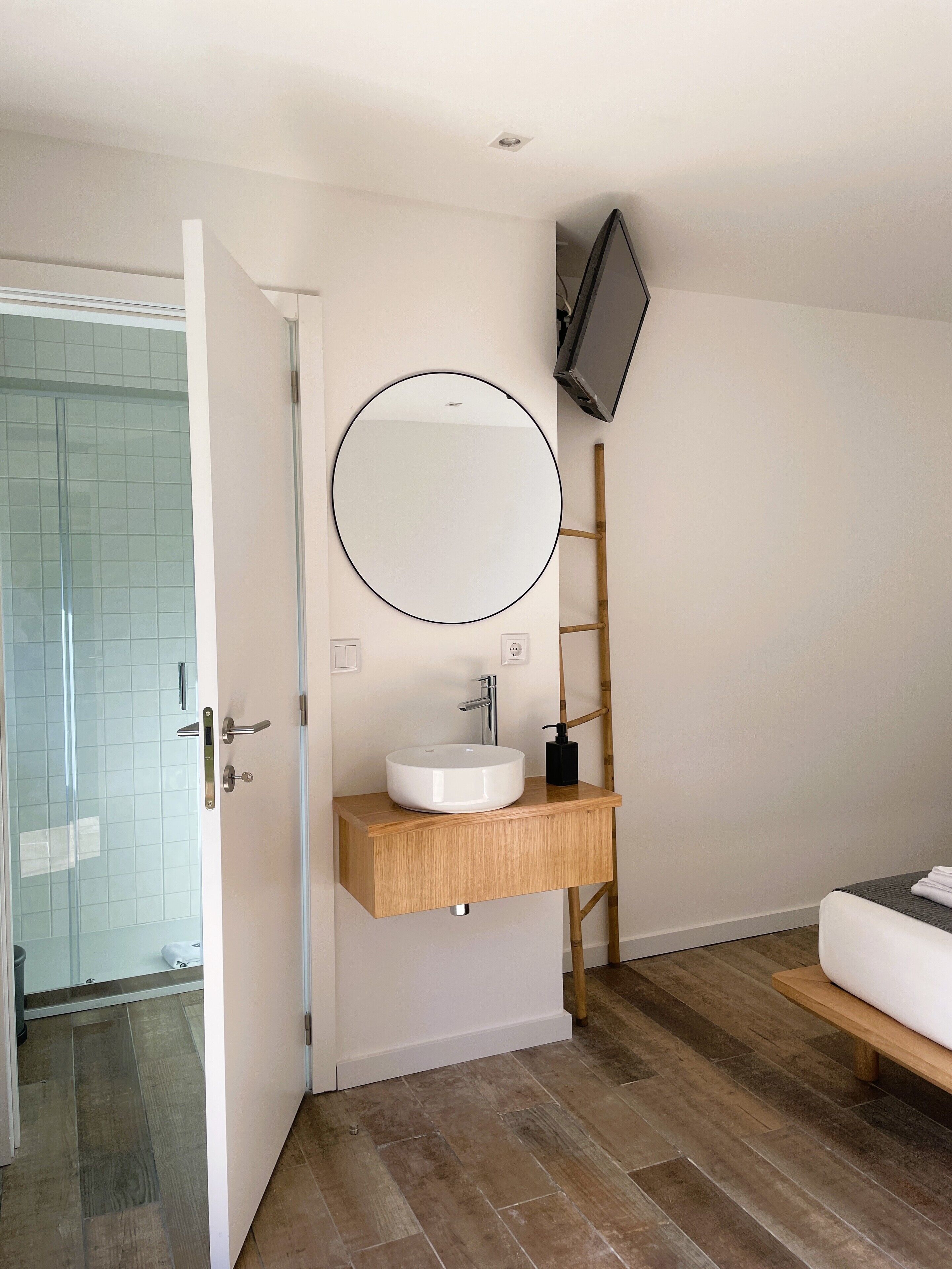 Une salle de bain moderne avec un miroir rond, un lavabo blanc et un meuble-lavabo en bois.