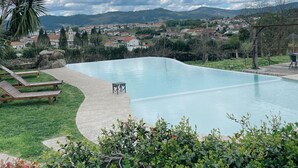 Una piscina con sillas de descanso y una pequeña mesa, rodeada de vegetación y con vistas a un pueblo y montañas al fondo.