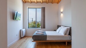 Un dormitorio con una cama, un televisor montado en la pared, un ventanal con vistas y un techo con vigas de madera.