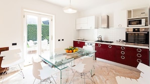 A modern kitchen with white cabinets, a glass dining table, and stainless steel appliances. - Villa Orlando with private pool - My Rental Homes (Sant'agnello)