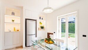 A modern kitchen with white cabinetry, a built-in refrigerator, and a glass dining table with a bowl of fruit. - Villa Orlando with private pool - My Rental Homes (Sant'agnello)