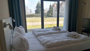 Et hotelværelse med to senge, et fjernsyn samt udsigt til en park og en bygning.