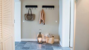 A hallway with a light-colored wall, a dark tiled floor, a coat rack with a bag and a jacket, a lantern, and a wicker basket. - Lexington RE-03 - The Lexington coach house RE-03 Holiday apartment with terrace on (Stolpe auf Usedom)