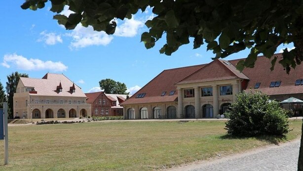 A courtyard with cobblestone paths, a grassy area, and a building with multiple windows and a red roof. - Lexington RE-03 - The Lexington coach house RE-03 Holiday apartment with terrace on (Stolpe auf Usedom)