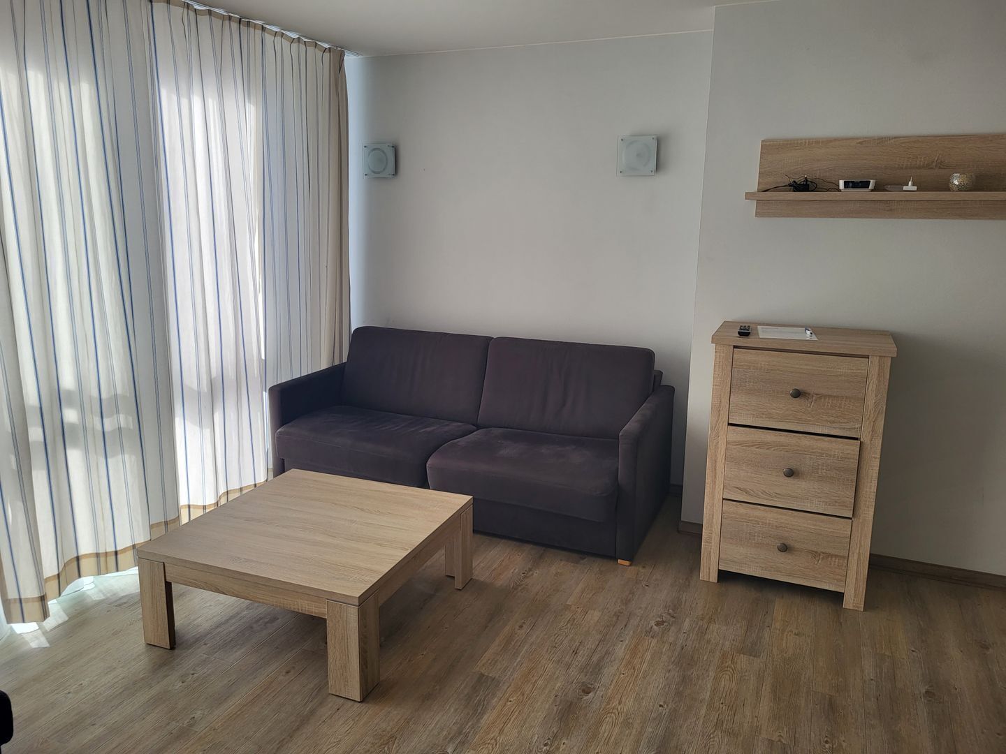 A modern living room with a dark brown sofa, a wooden coffee table, and a wooden dresser with drawers.