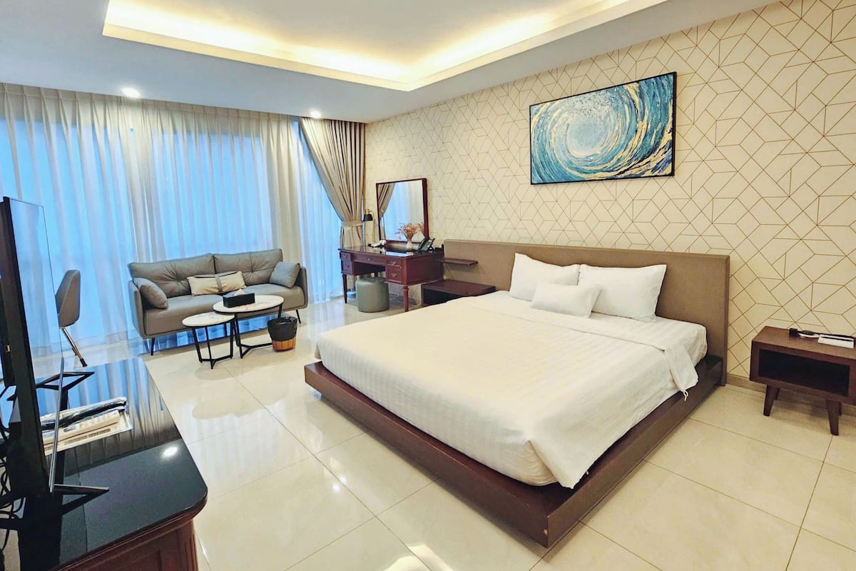 Quarto de hotel moderno com uma cama grande, um sofá, uma escrivaninha e uma televisão.