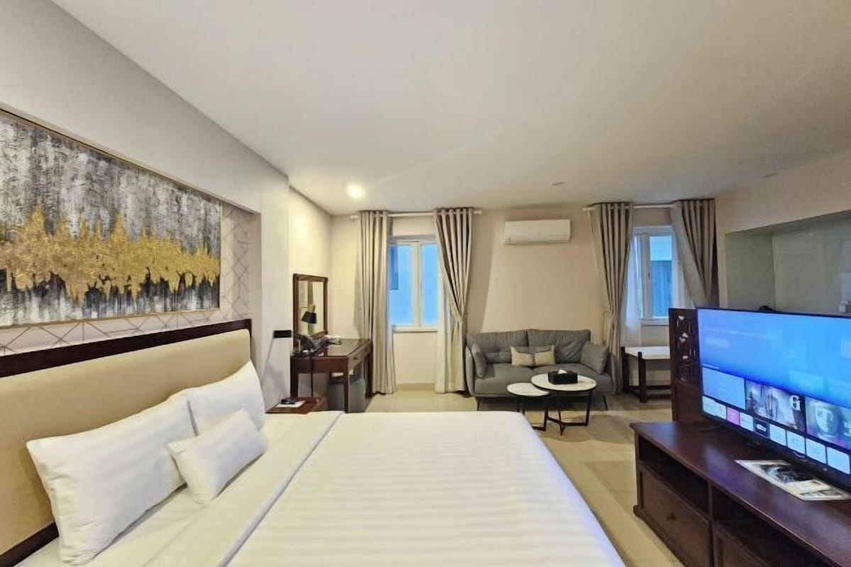 Een hotelkamer met een groot bed, een televisie, een bureau, een stoel en een schilderij aan de muur.