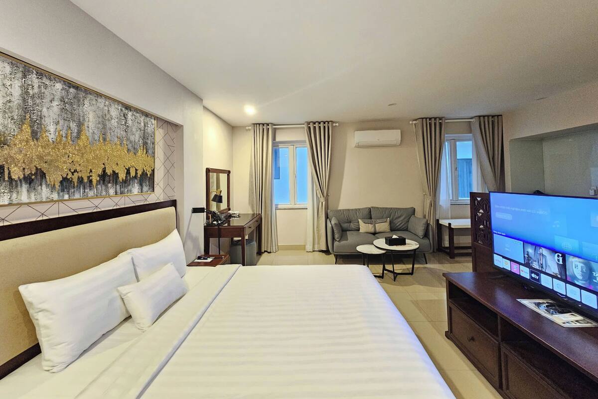 Quarto de hotel com uma cama grande, uma mesa com cadeira, uma televisão e um quadro na parede.