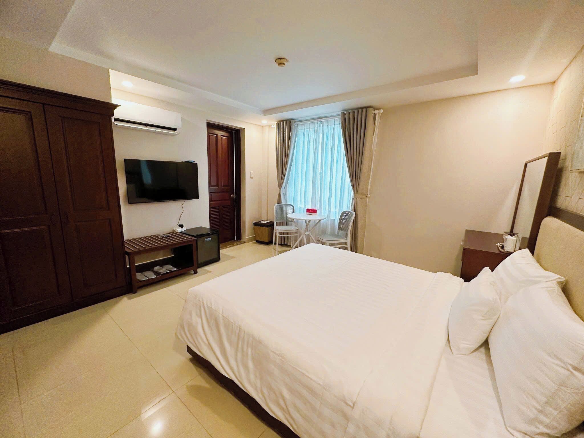 A hotel room with a bed, a TV, a desk, a chair, and a window with curtains.